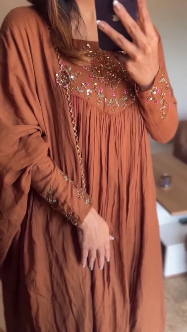 This is a stunning brown kurta with delicate embroidery around the neckline and sleeves. The outfit’s flowy silhouette paired with the graceful pleats
